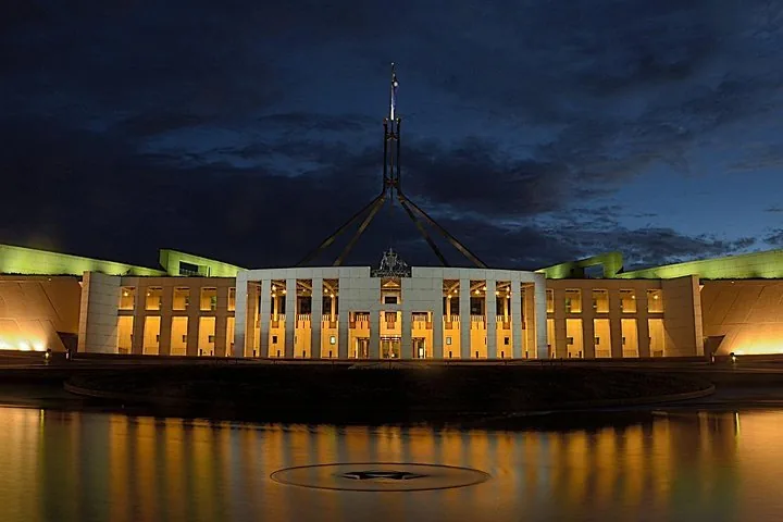 Das beleuchtete Parliament House bei Nacht mit einer Fahne darüber.