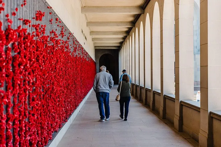 People walking along a colonnade beside a poppy wall.